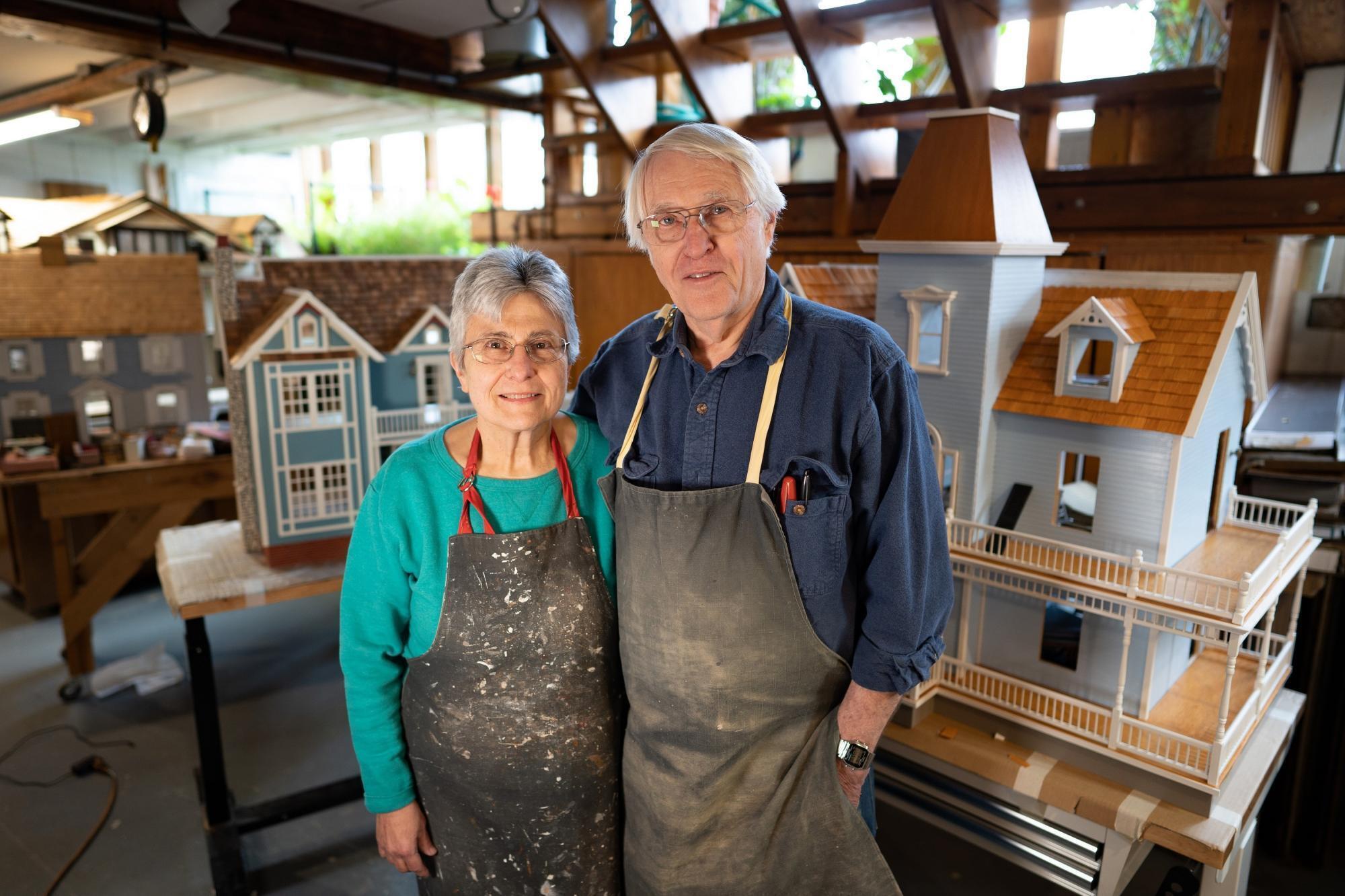 Sharon and Norm Ewert stand in front of wooden dollhouses.