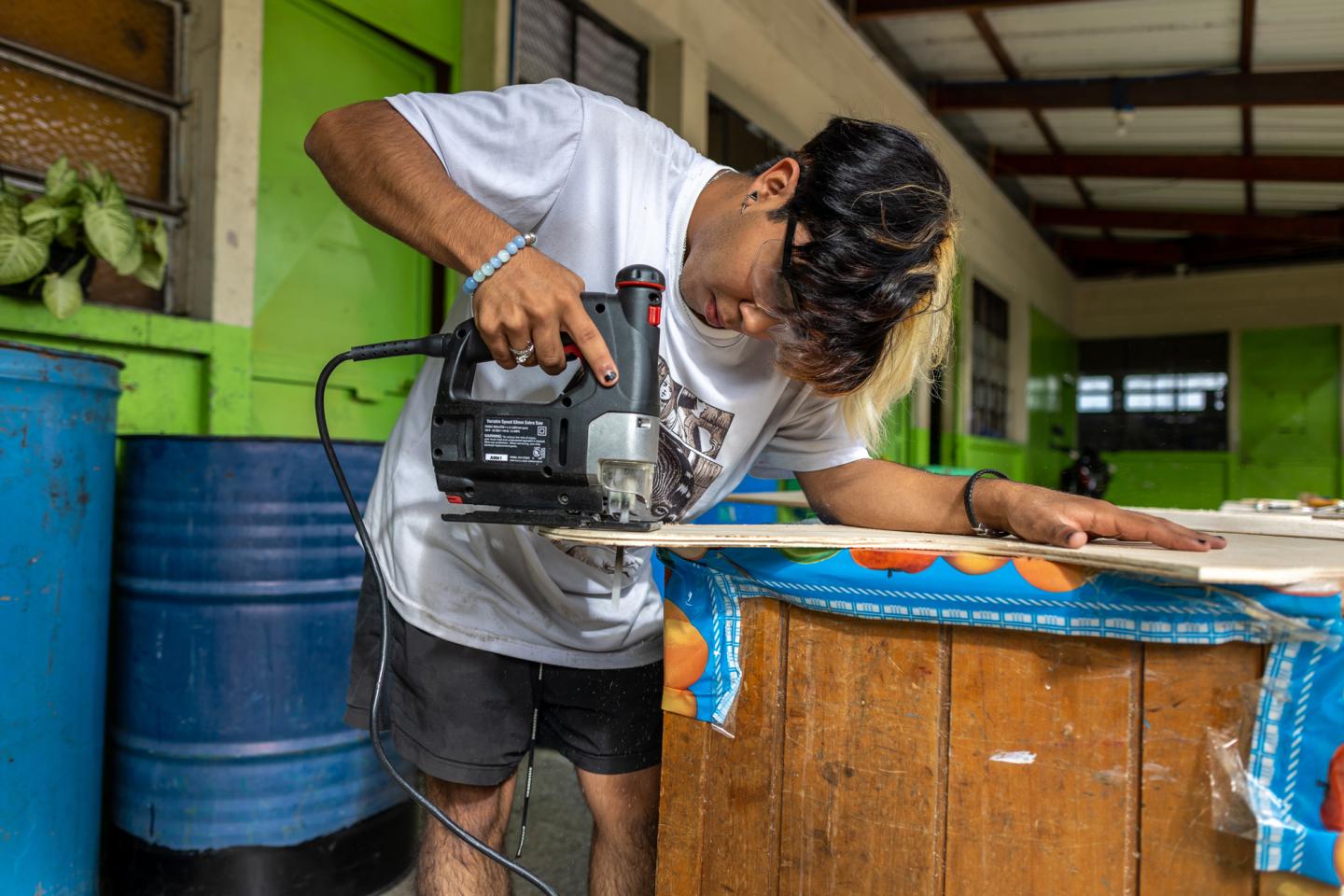 Julio Lopez cuts pieces of wood to replace the rotting parts of desks at the school.