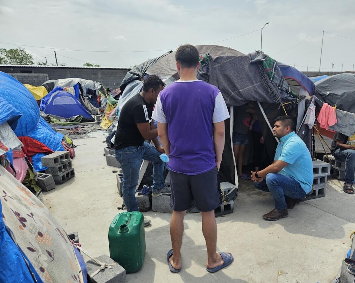 Man sitting in front of tent in informal settlement talking to others