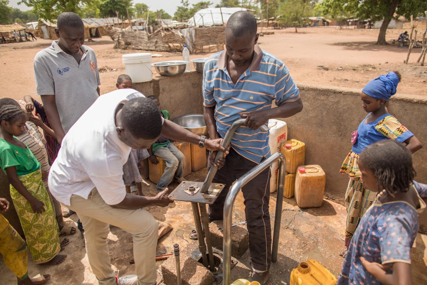 Two Chadian men work on a water pump while several children watch