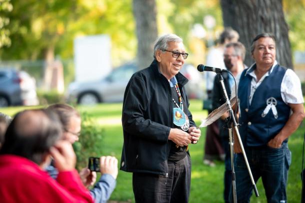 An Indigenous elder speaks into a microphone during an outside event.