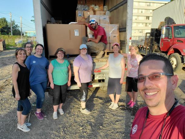 Nine people pose in front of an open trailer filled with boxes