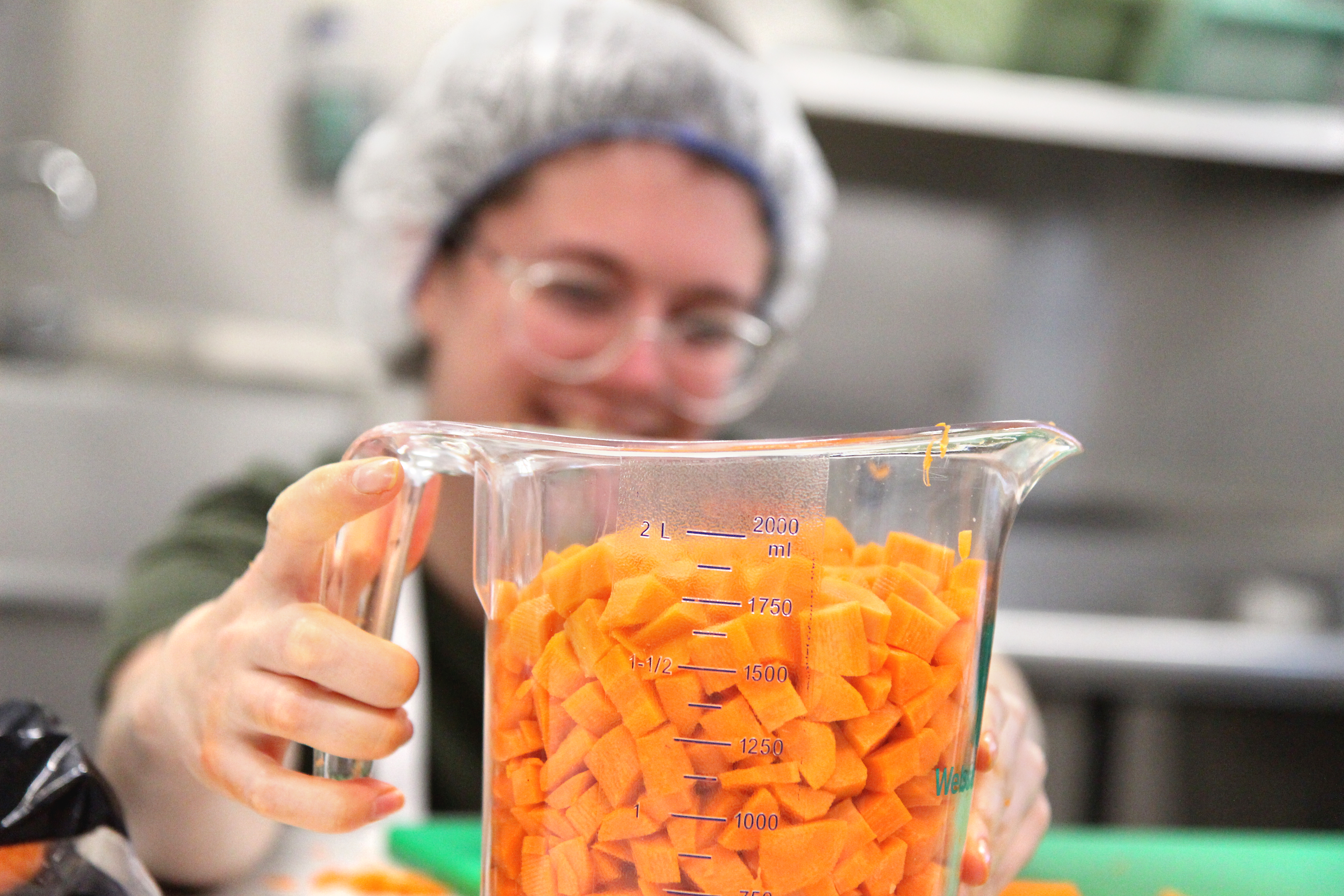 A person holding up a measuring cup filled with chopped carrots