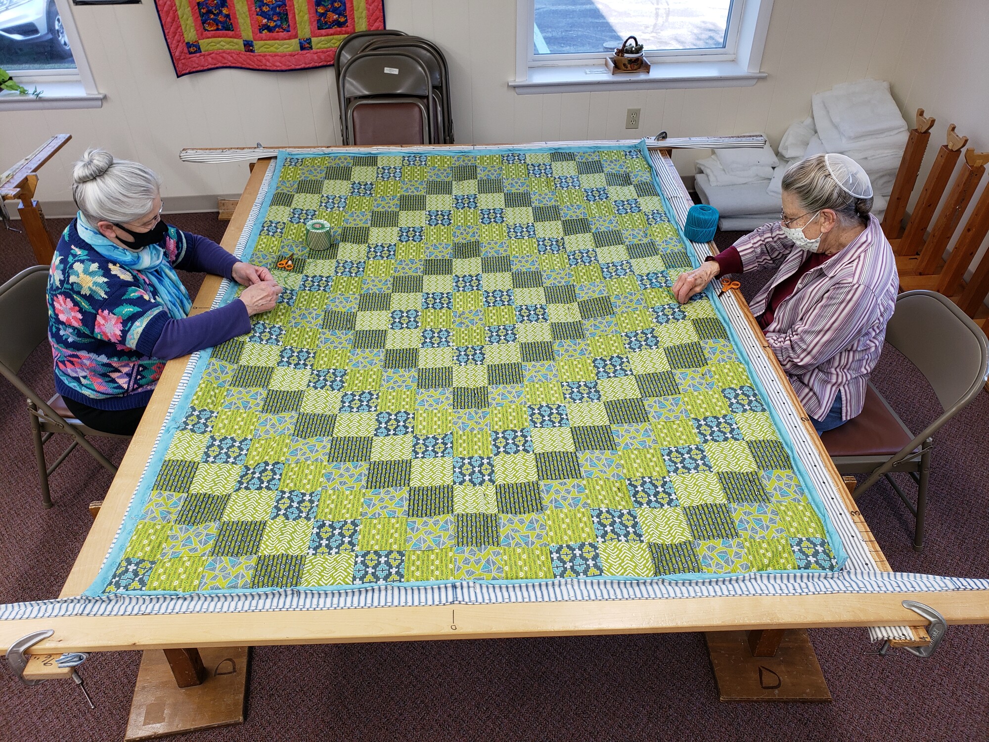 Two women stitching a green quilt