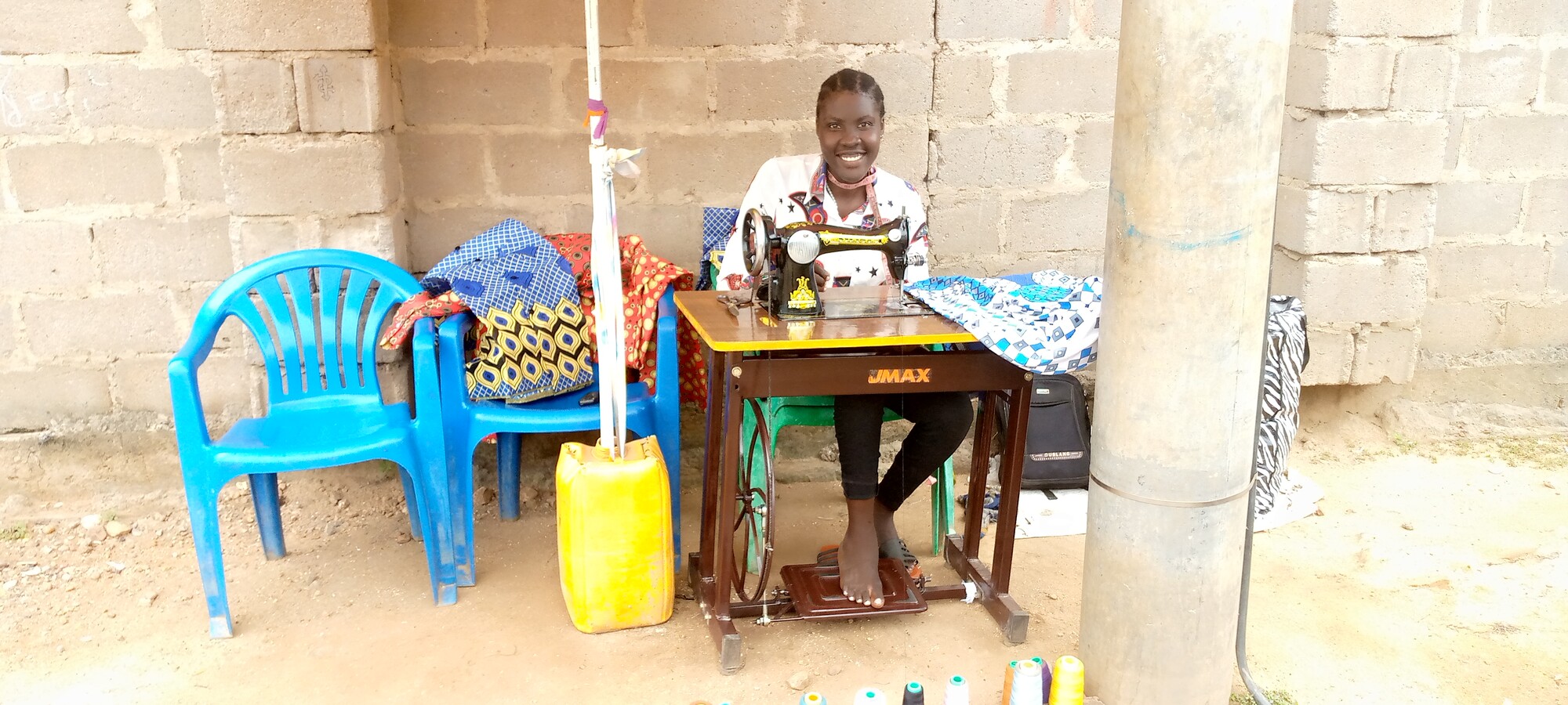 A person sits at a sewing machine and smiles at the camera