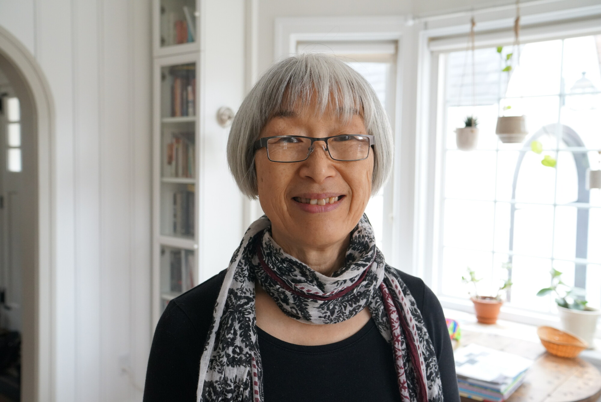 A portrait of an older woman with short grey hair, glasses, wearing a scarf