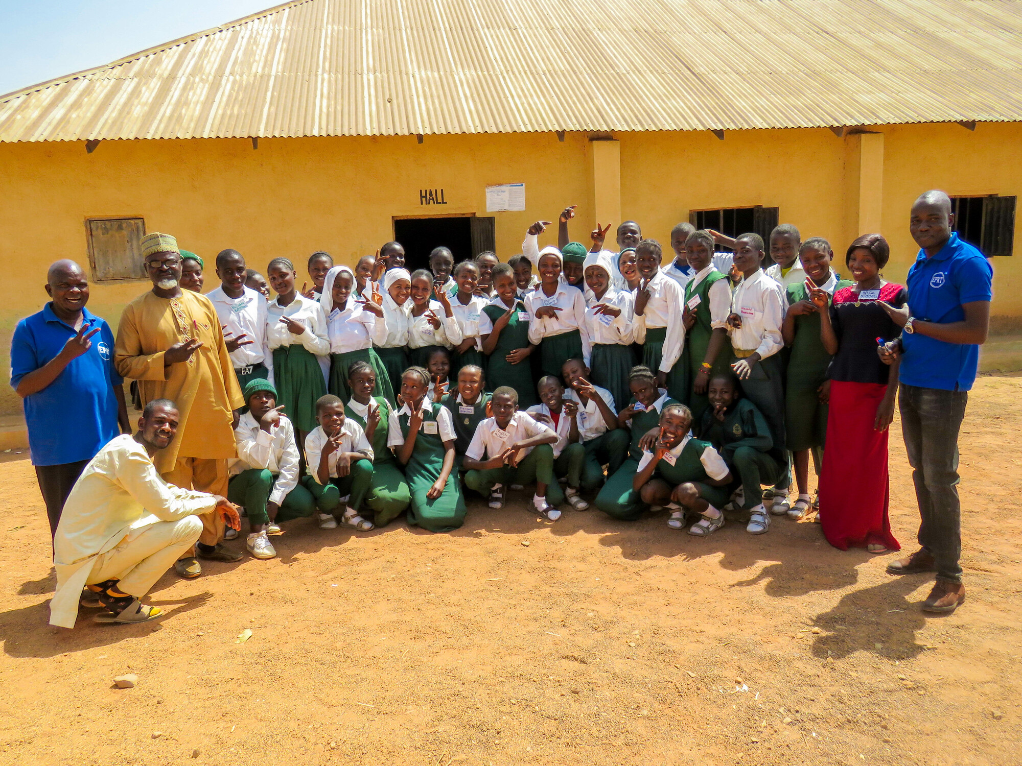 A group of students and teachers standing for a photo in front of a school