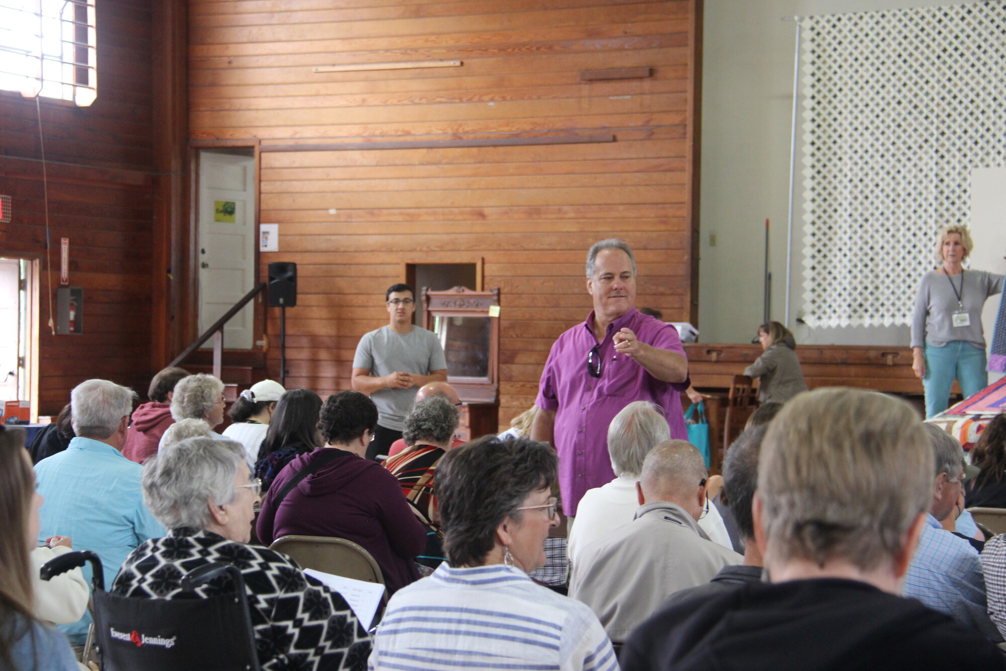 An auctioneer in a purple shirt stands in front of a crowd