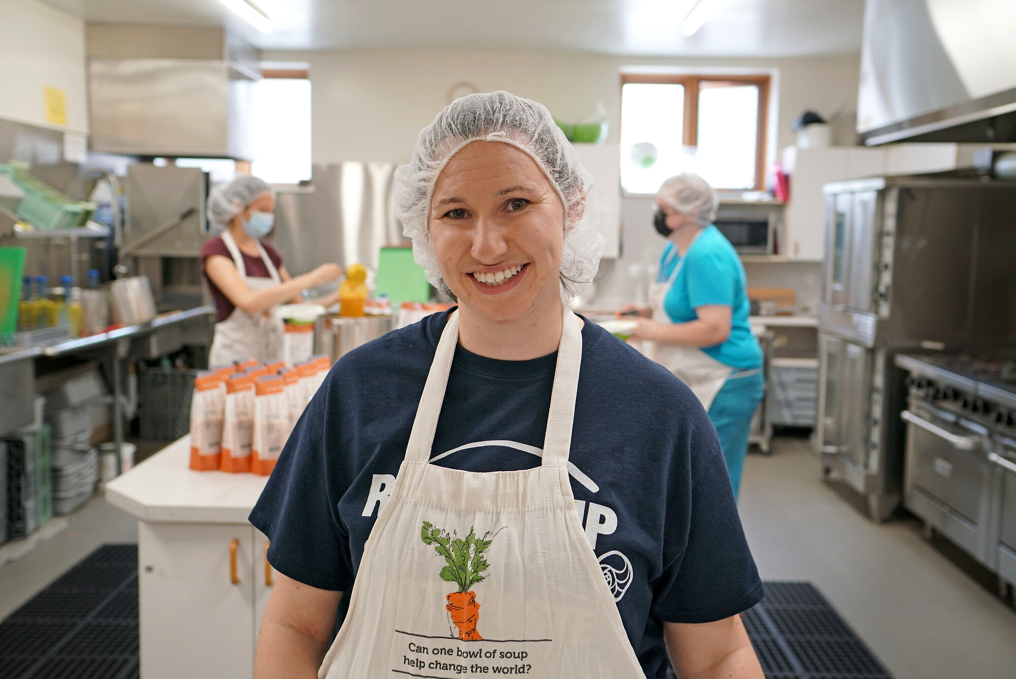 Smiling woman wearing an apron in a commercial kitchen.