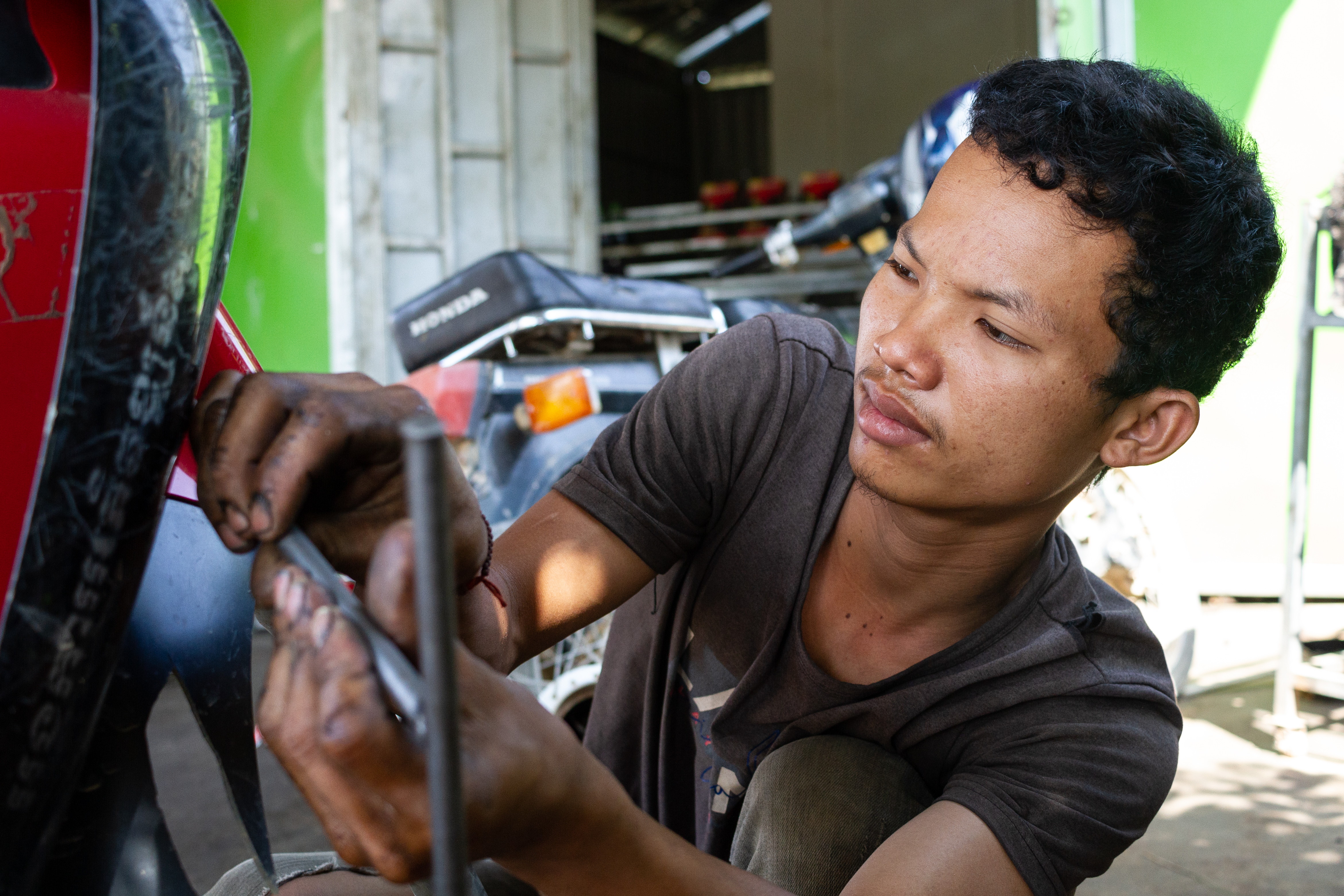 Hun Rortha works on a motorbike's suspension at his motorbike and engine repair shop in Ba Phnom district, Cambodia. Hun Rortha is a graduate from MCC partner Organization to Develop Our Villages' (ODOV) vocational training program, and using the skills and knowledge he gained during that training opened his own shop in 2021.