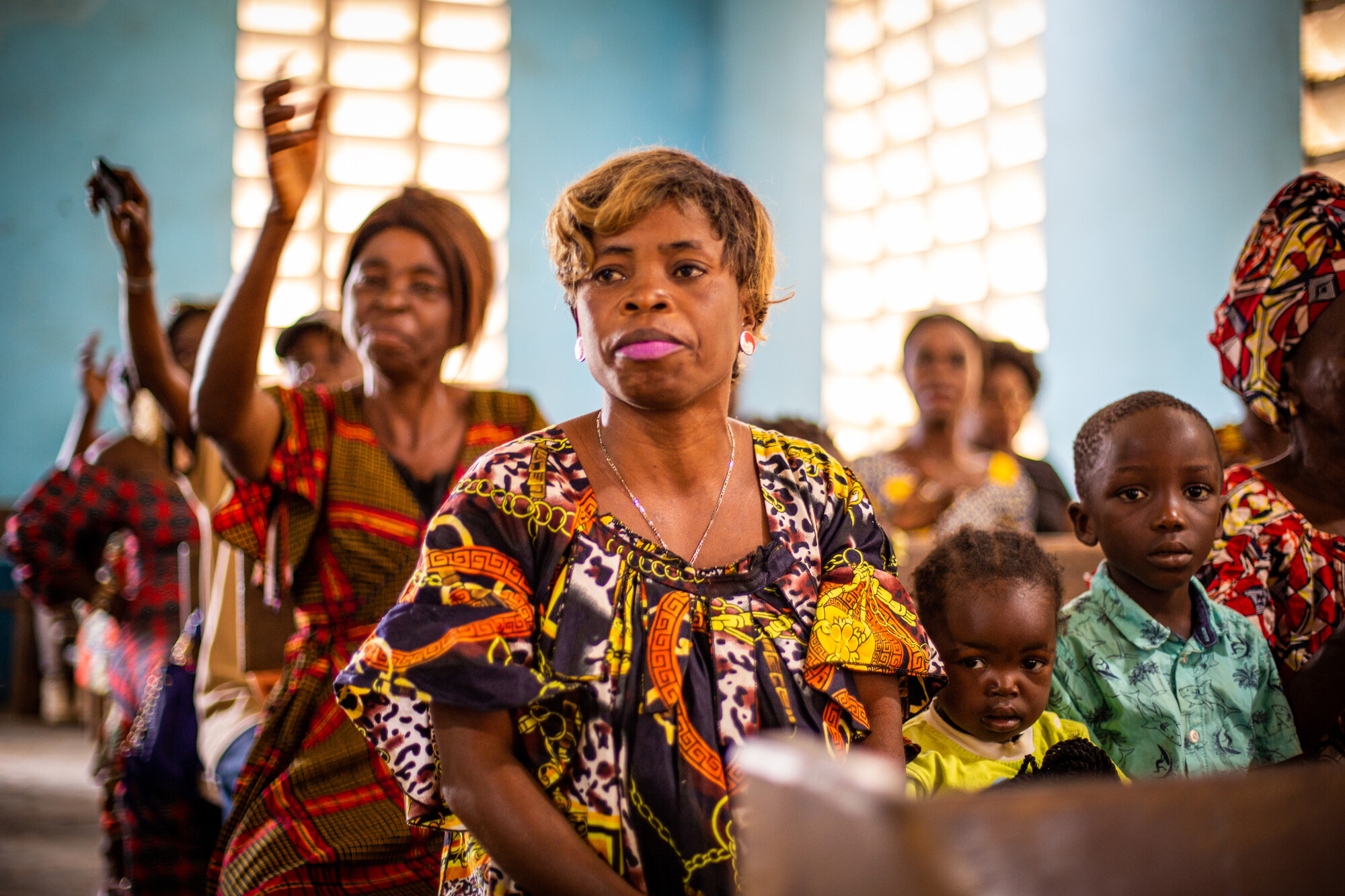 A Congolese woman sits in a church pew. Next to her are two children