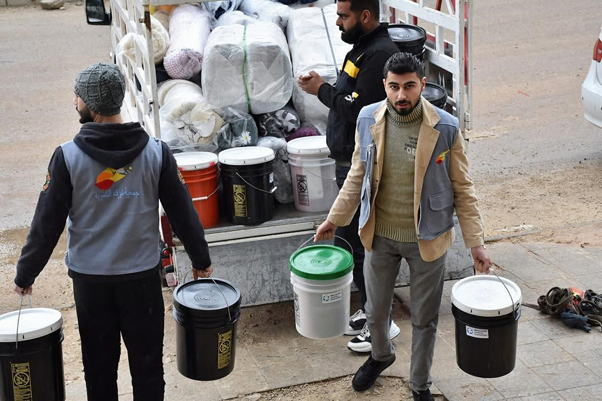 Three men unloading relief kit buckets and comforters from the back of a truck