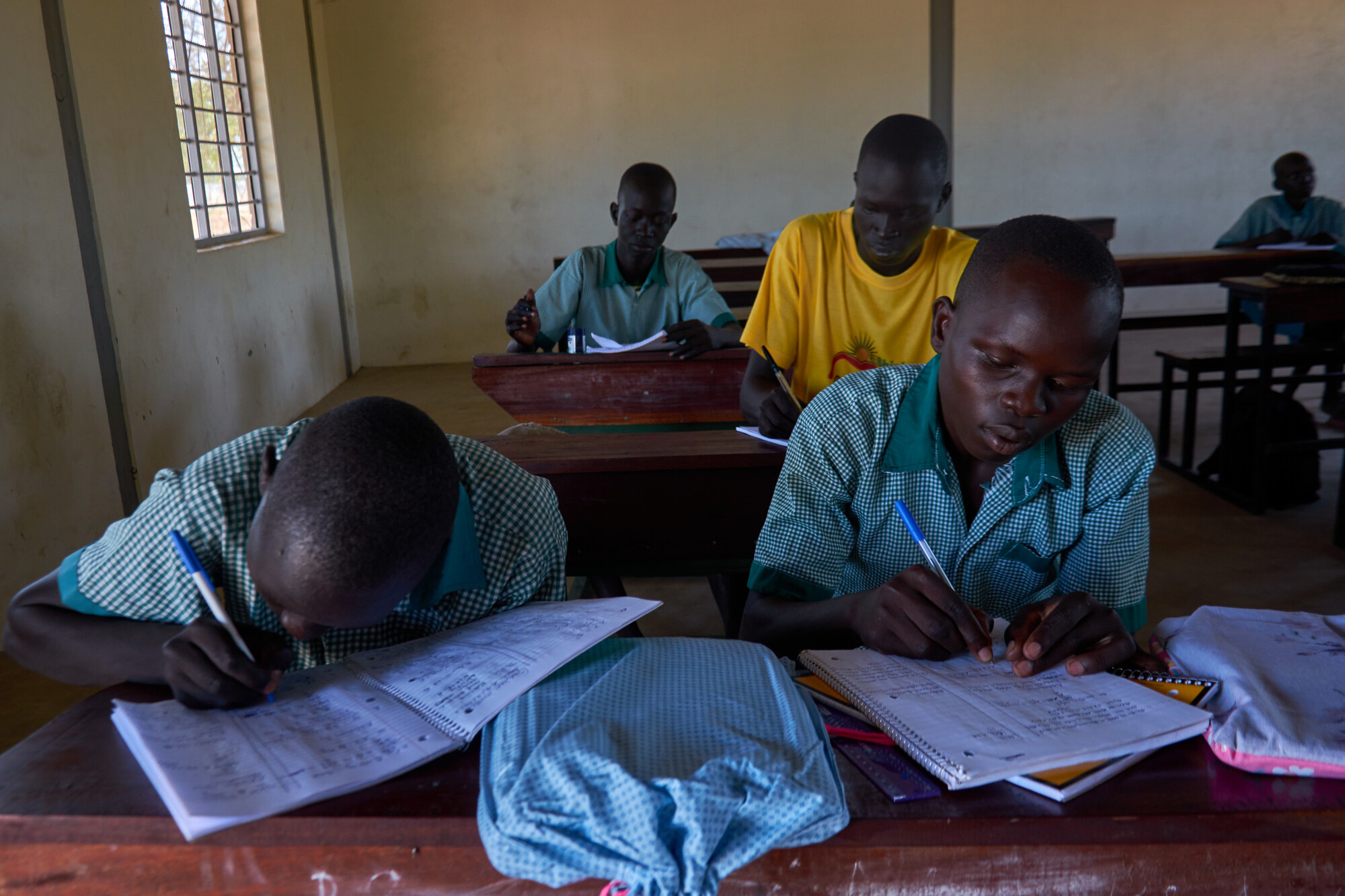 Two South Sudanese students write in notebooks while sitting at a desk