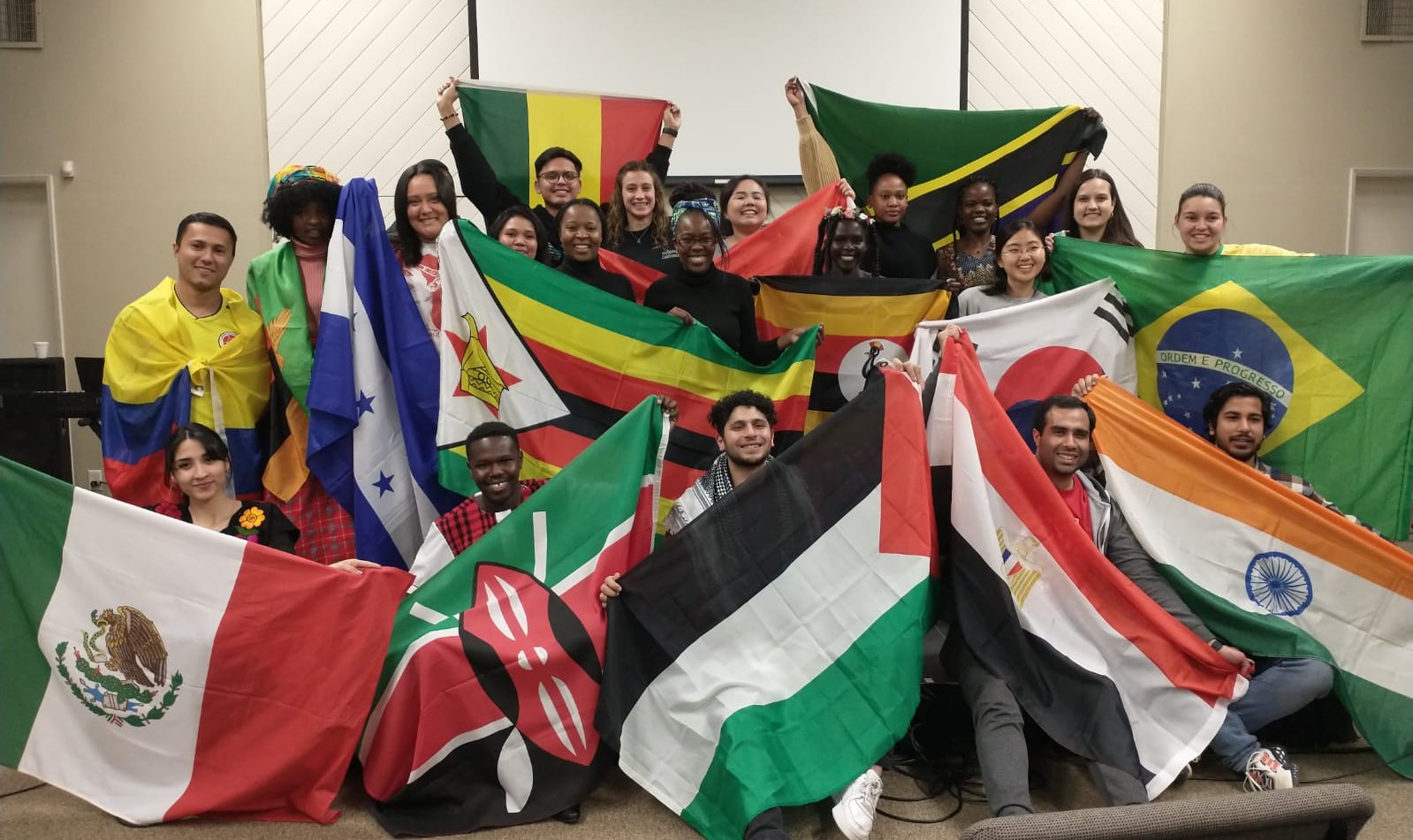 A large group of young adults pose for photo. They are holding different country flags.