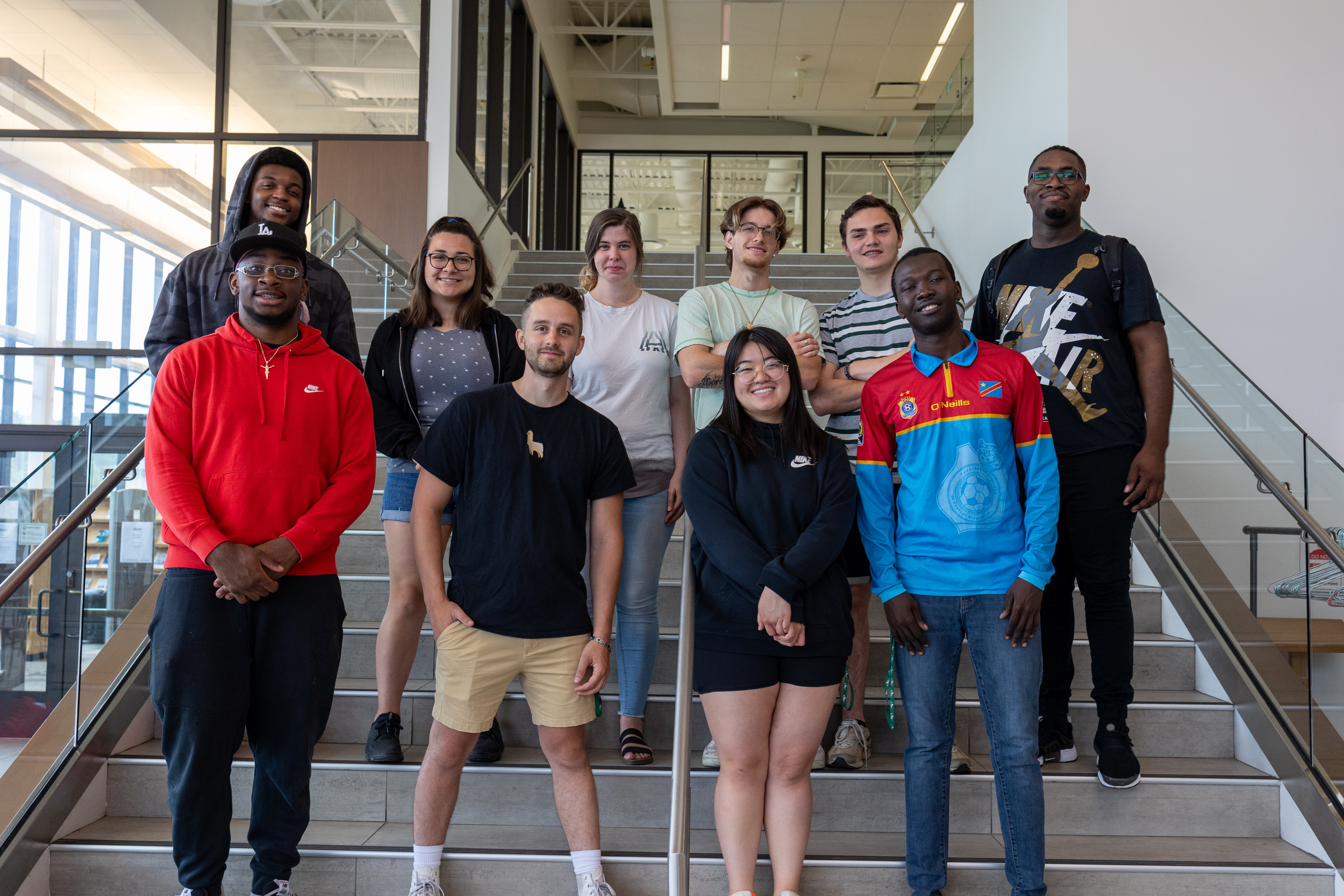 Ten young adults stand together for a group photo on a set of stairs.