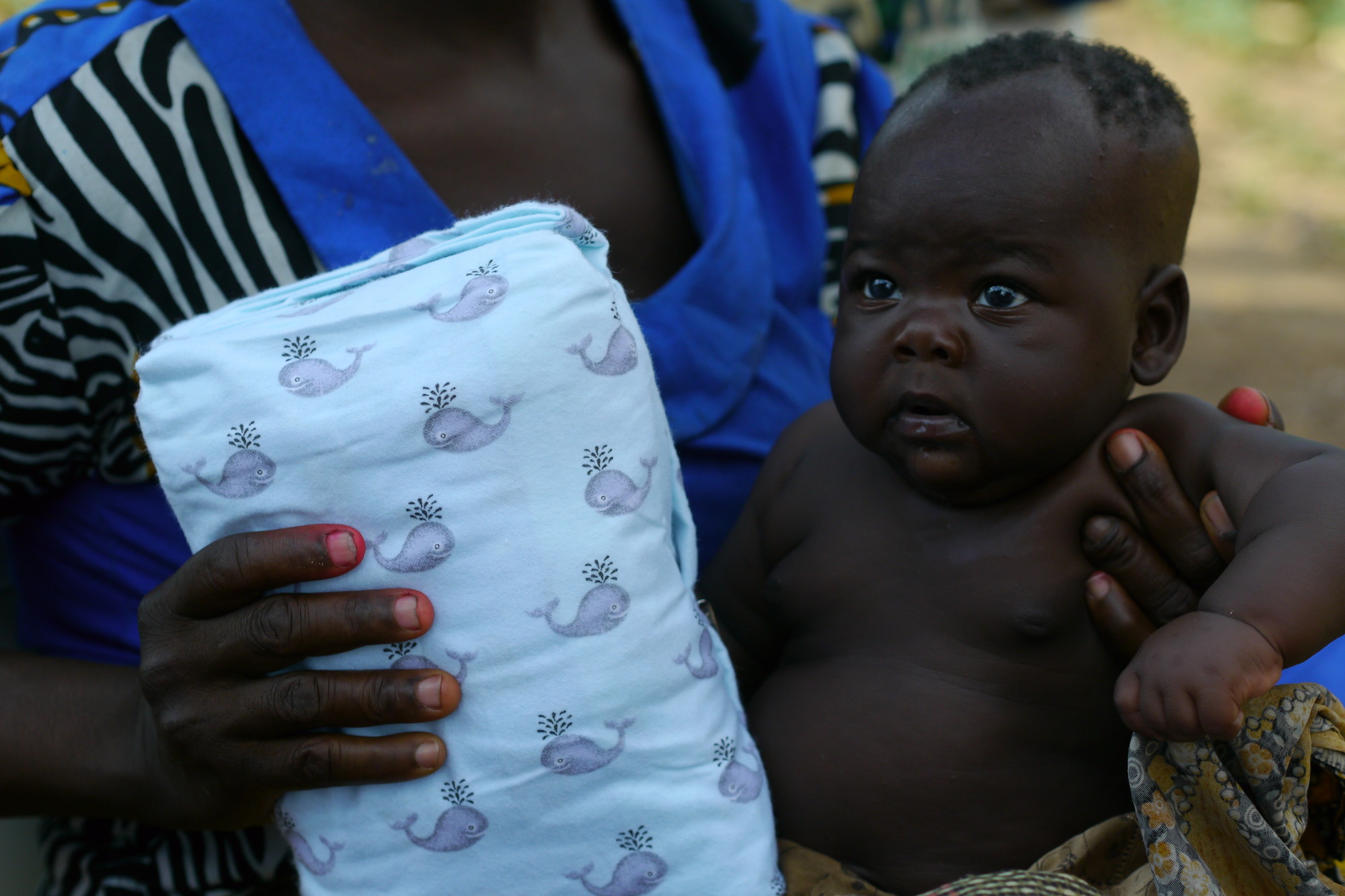 A person holds a baby on her lap while also holding a bundle of fabric