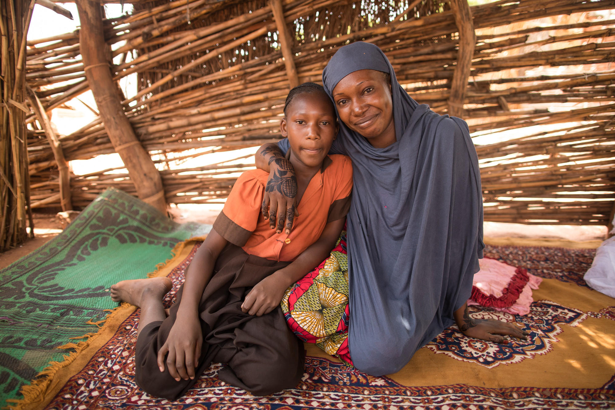 A woman and young girl sitting inside a shelter smiling for a photo