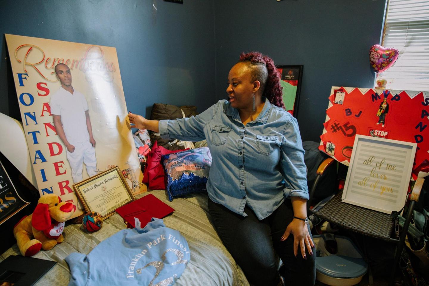 A woman sits on a twin bed and touches a poster picturing a young adult.