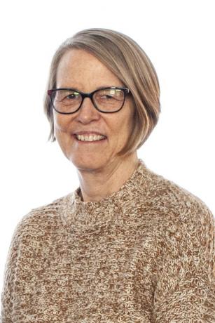 Portrait of a woman with short, light hair, glasses and a brown sweater