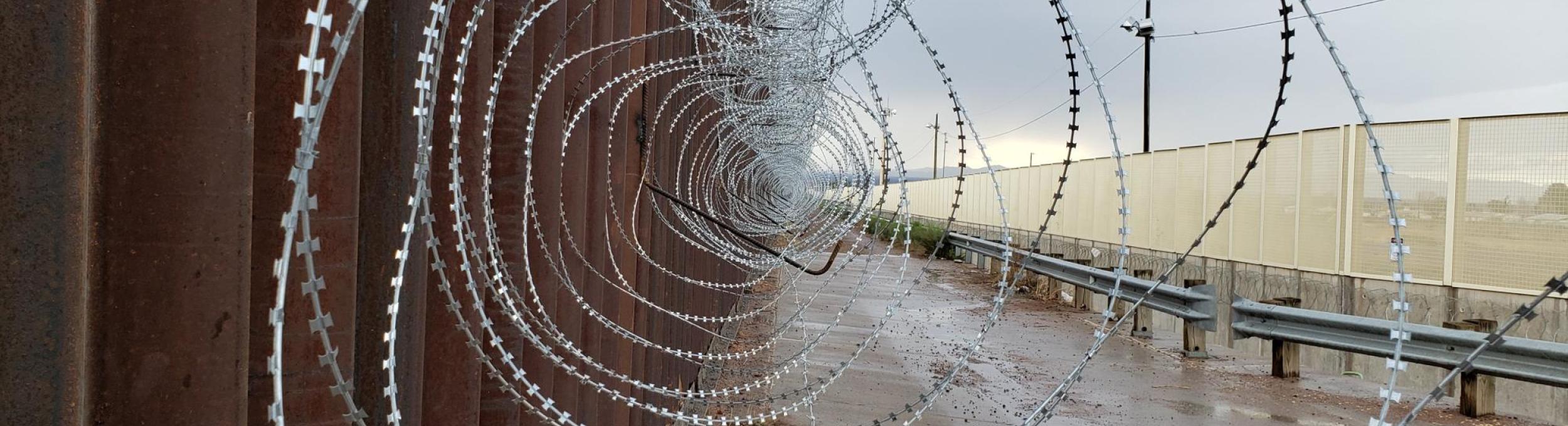 Looking through a coil of barbed wire at a border wall