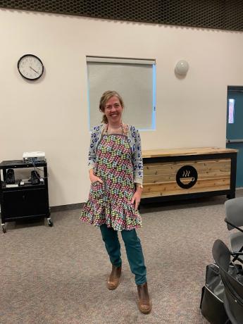 A woman stands and shows off the apron she is wearing.