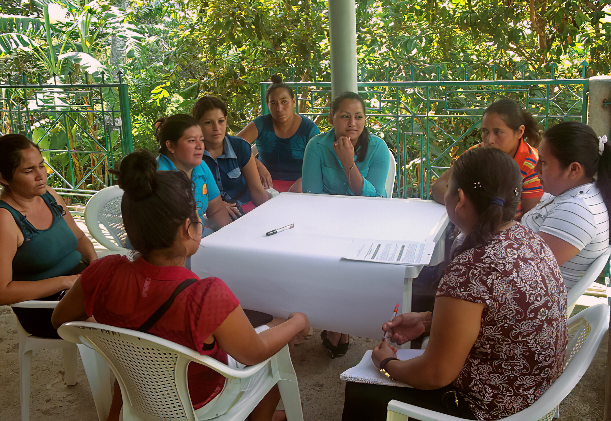 Nine Salvadoran woman sit around a table with a giant piece of paper on it
