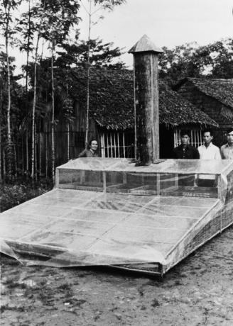 A black and white photo featuring four people standing behing a large piece of machinery