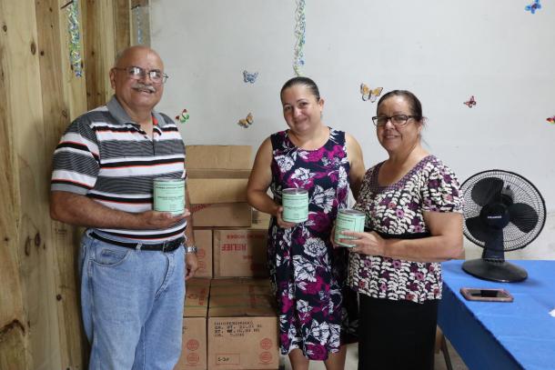 Three people stand holding a green tin can