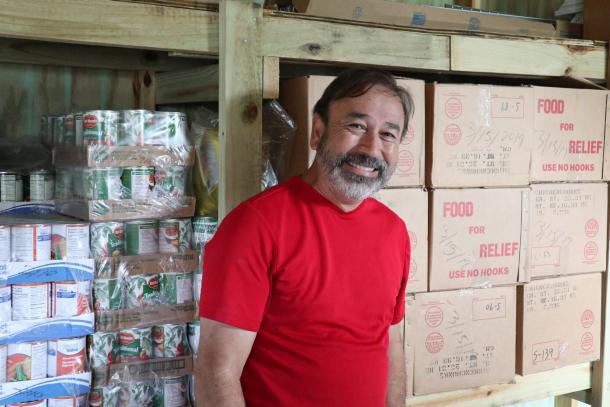 A man in a red shirt stands in front of bulk food supplies and boxes