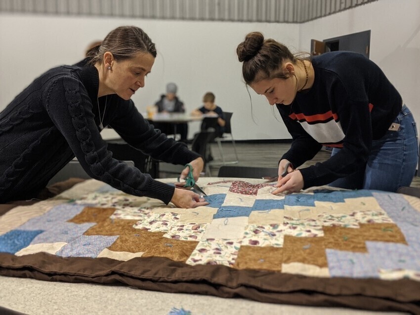 Two women lean over a comforter top they are working on.