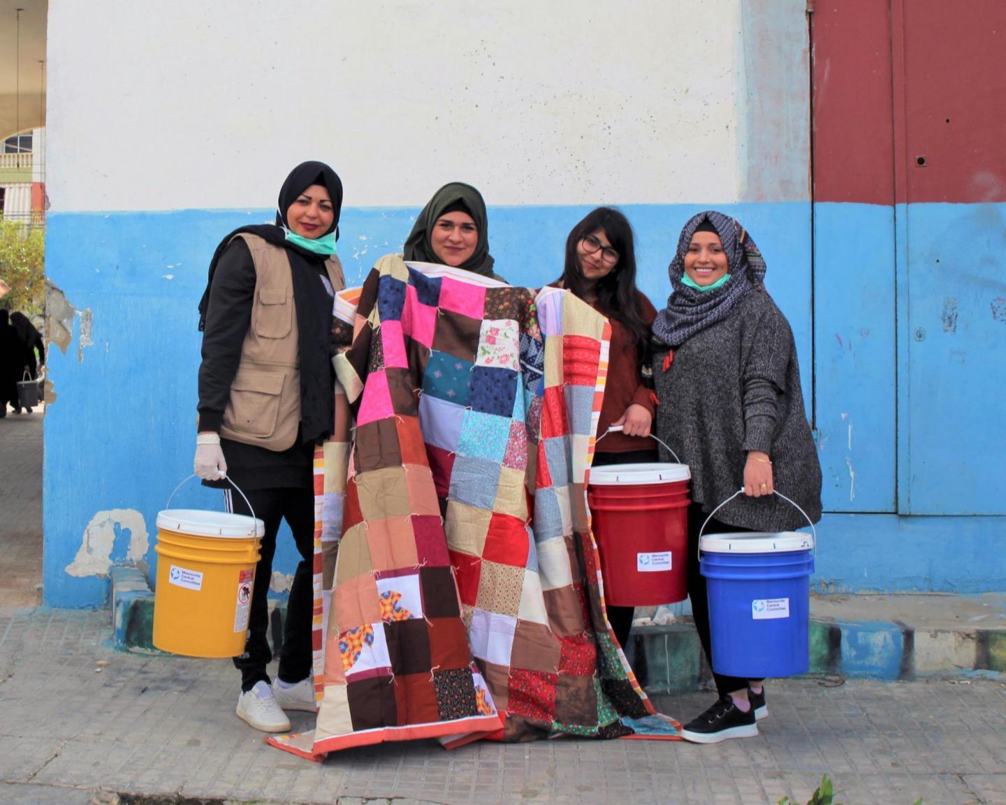 Four women stand together and pose with a comforter and three five-gallon buckets.