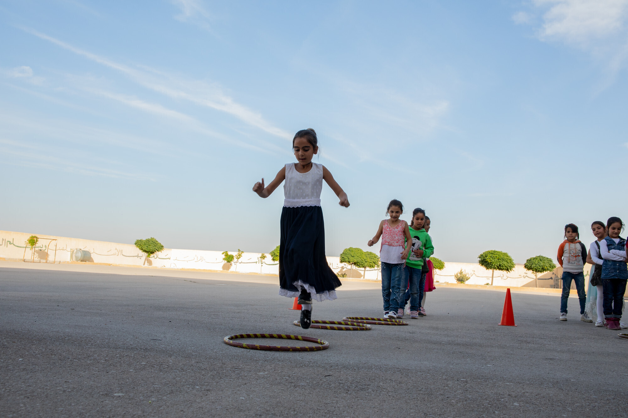 Children jump in and out of hula hoops which are laying on the ground 