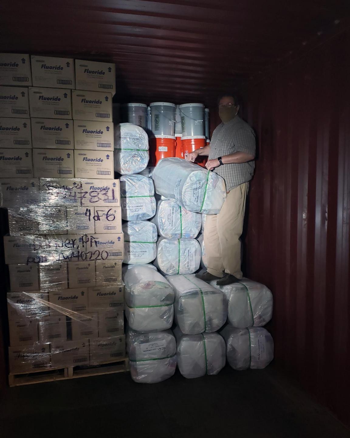 A man in a face mask packs a shipping container with boxes, bales and buckets