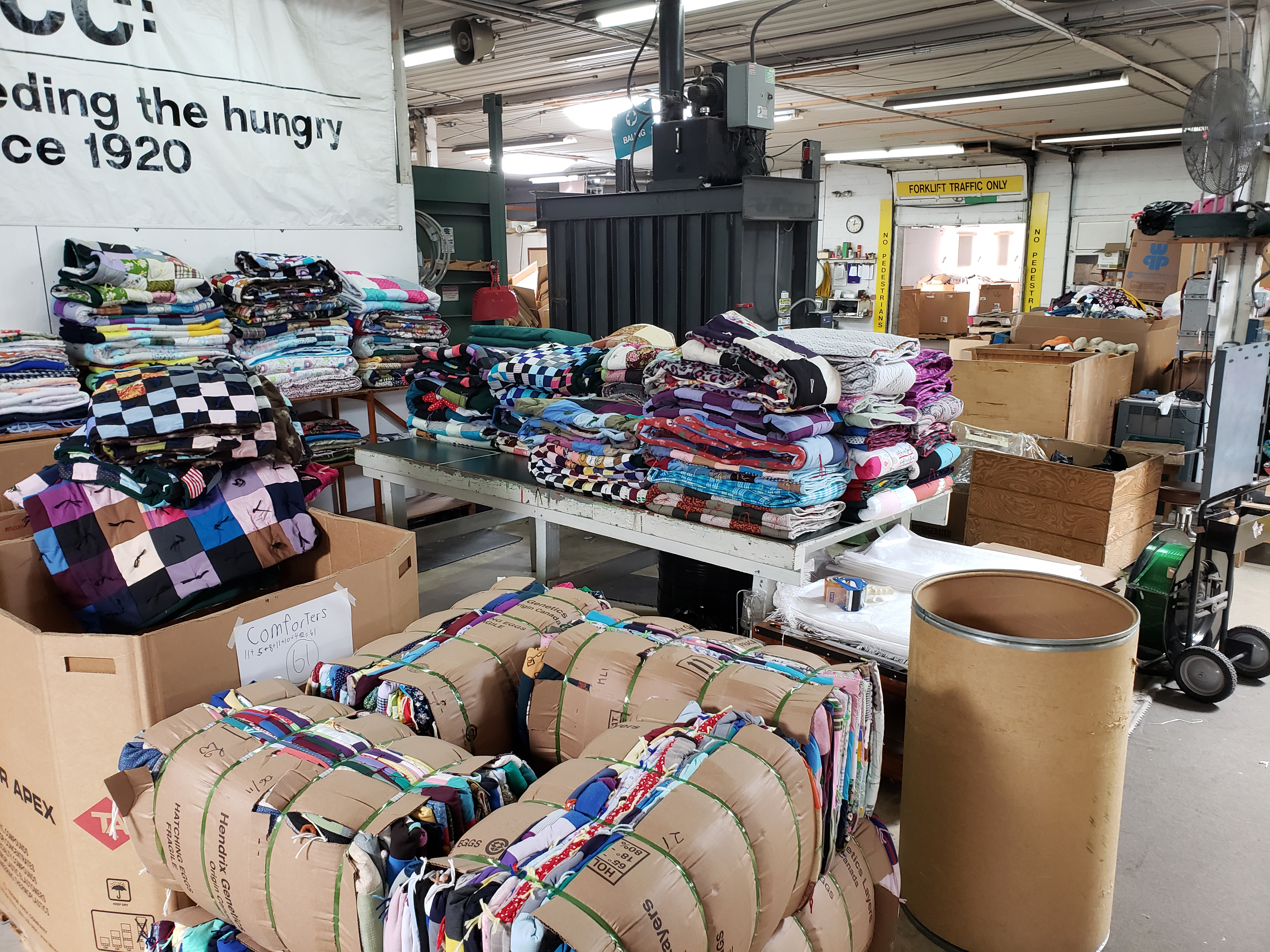 A number of piles of folded comforters sit on different surfaces in a warehouse.