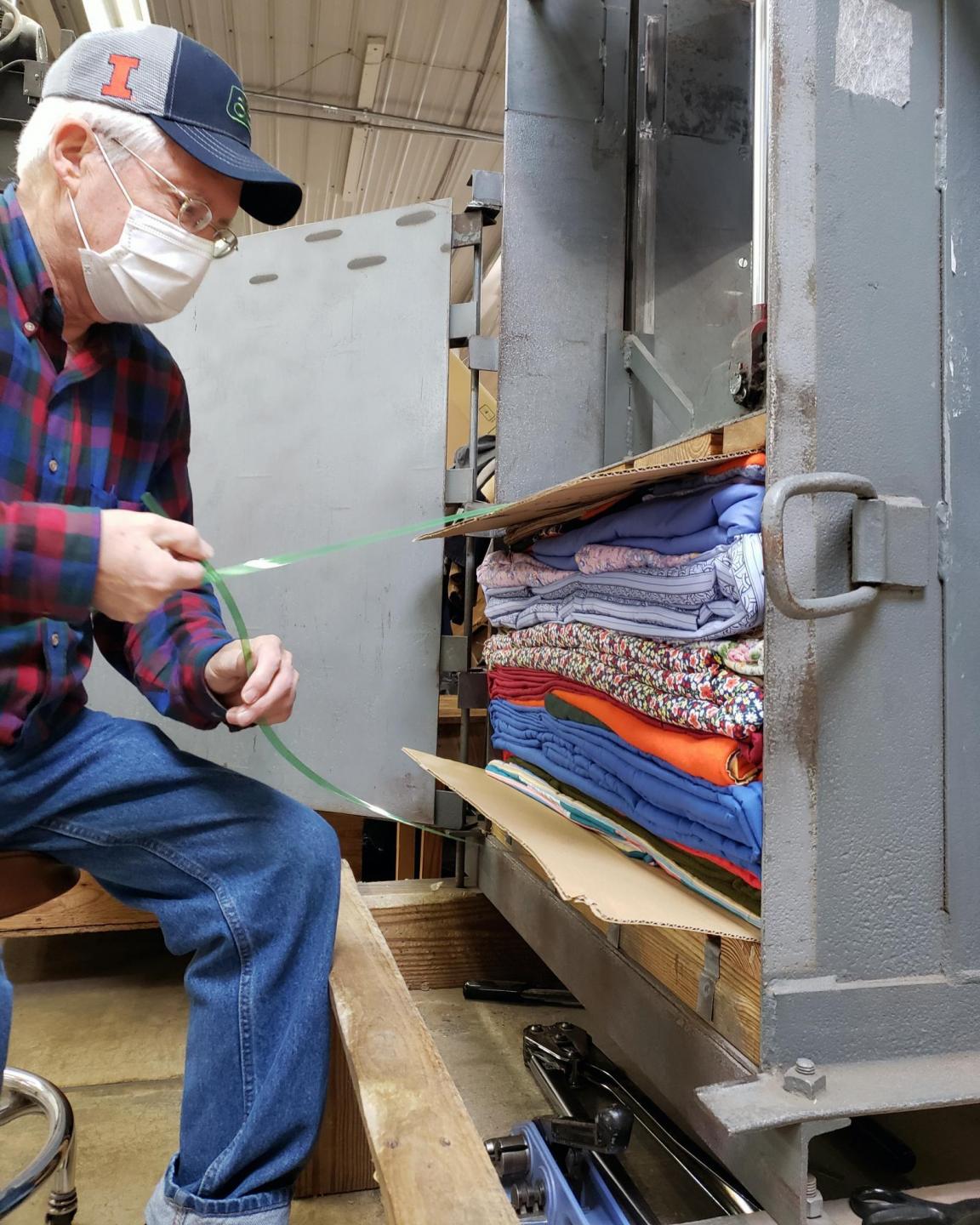 A man ties a bale of comforters sitting in a baler.