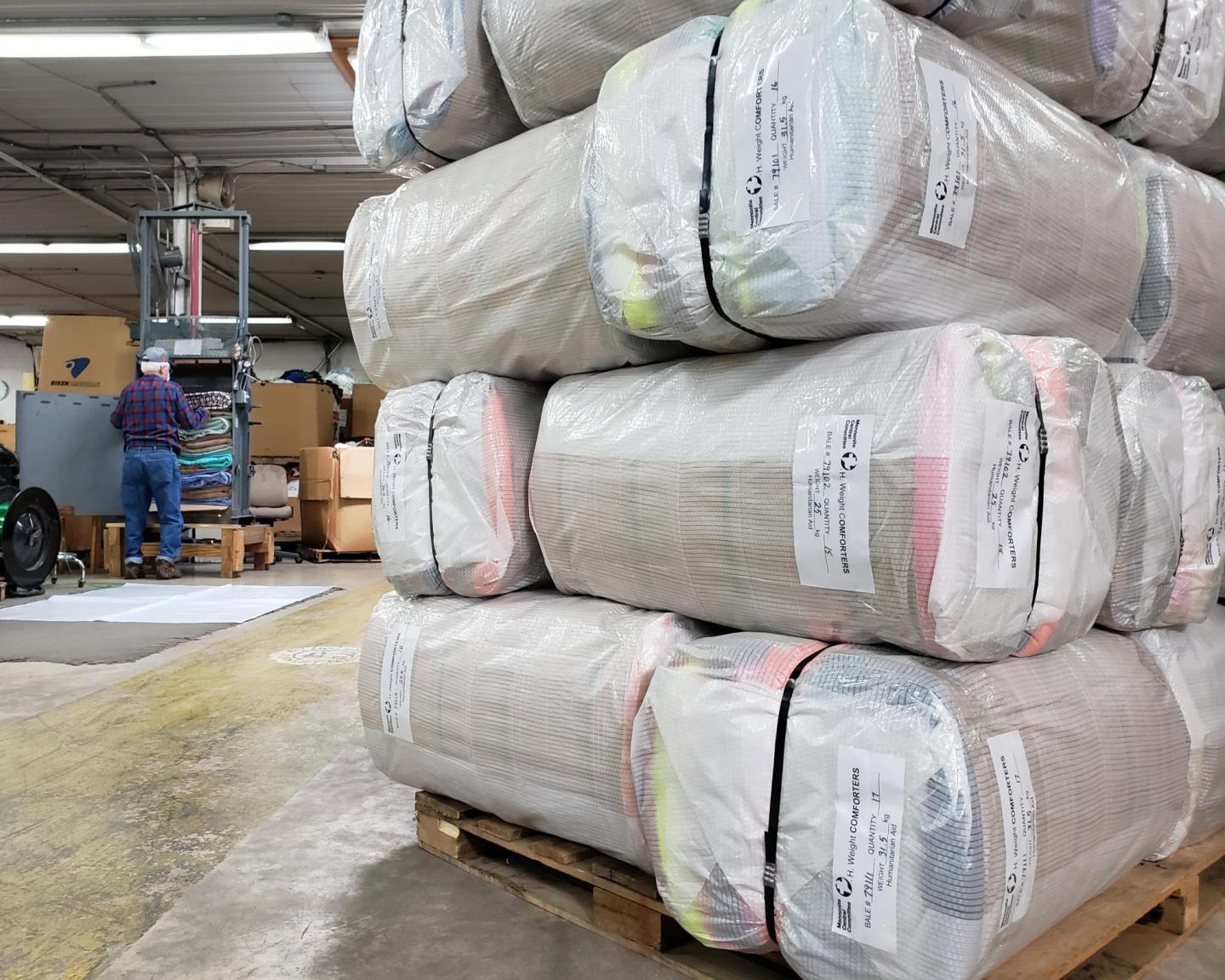 A pile of neatly stacked bales wrapped in plastic sit on a pallet in a warehouse.