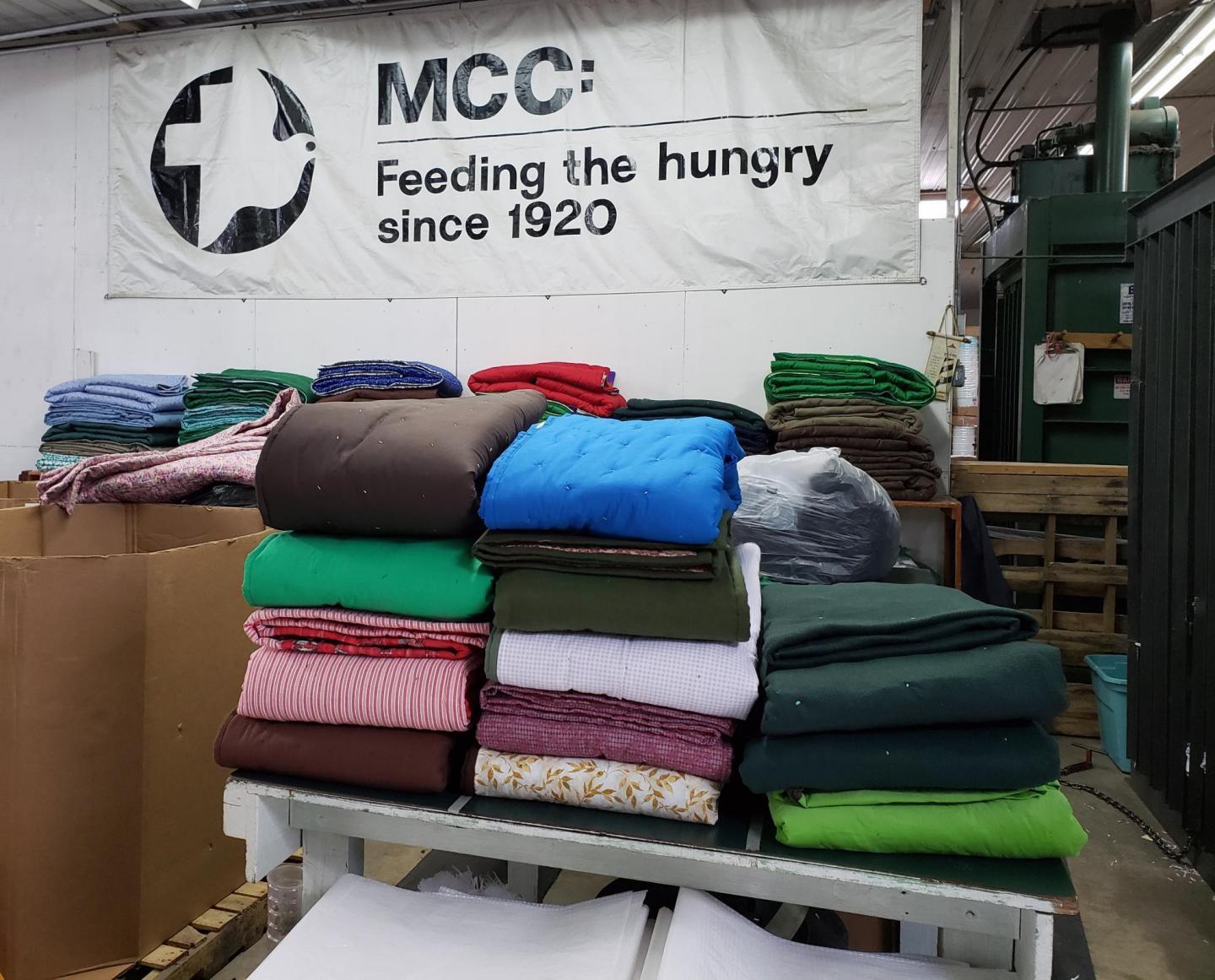 Piles of folded comforter on a tabletop in a warehouse.