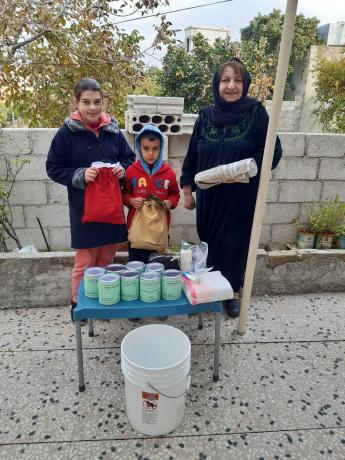 A woman and her two young grandchildren (names not provided for security reasons) received MCC kits and canned meat from MCC partner Fellowship of Middle East Evangelical Churches in November 2020. These items were part of larger shipments of MCC humanitarian assistance for displaced Syrians and vulnerable host communities.