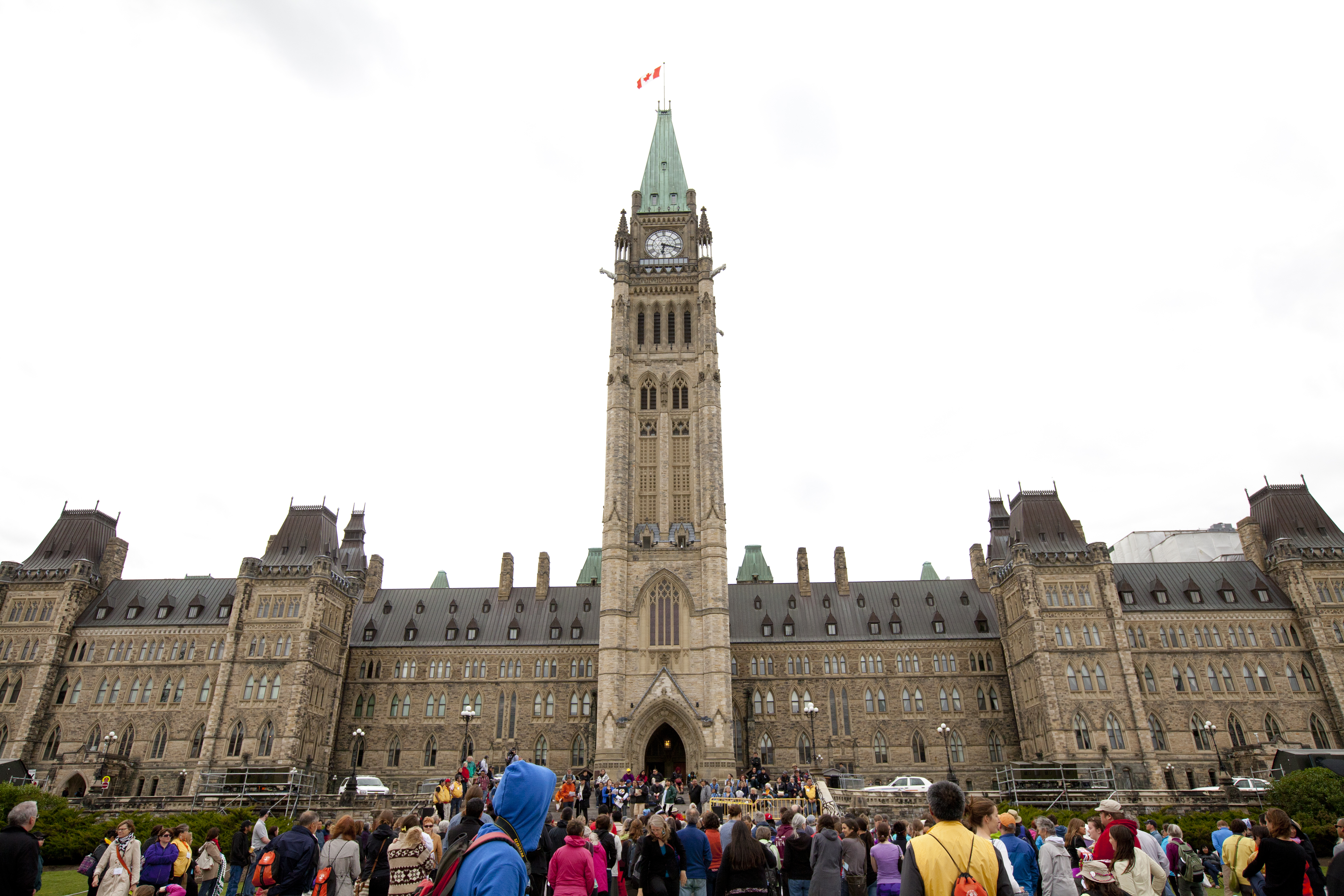 A crowd of people stand in front of Parliament Hill in Ottawa