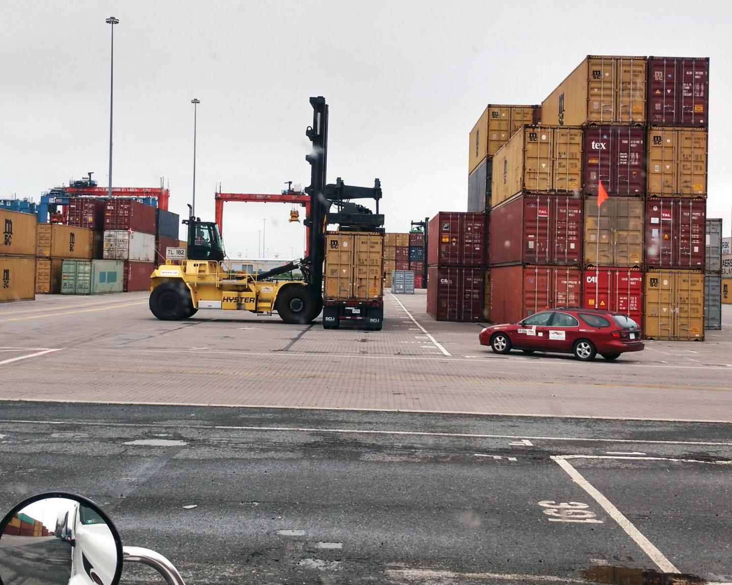 A container being placed on a pile of other shipping containers at a port.