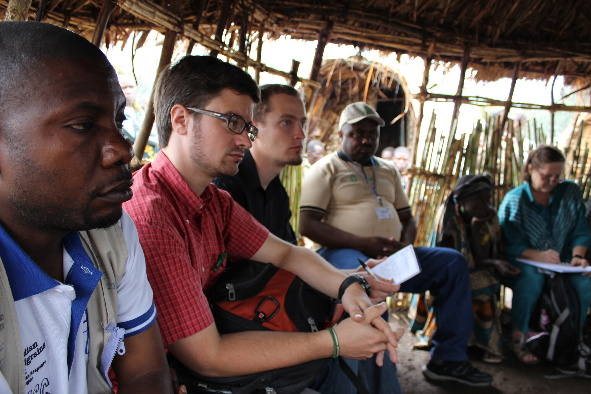 A group of people sit in a hut listening to someone speaking out of view.