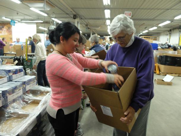 A young woman puts cans into a box that an older man is holding