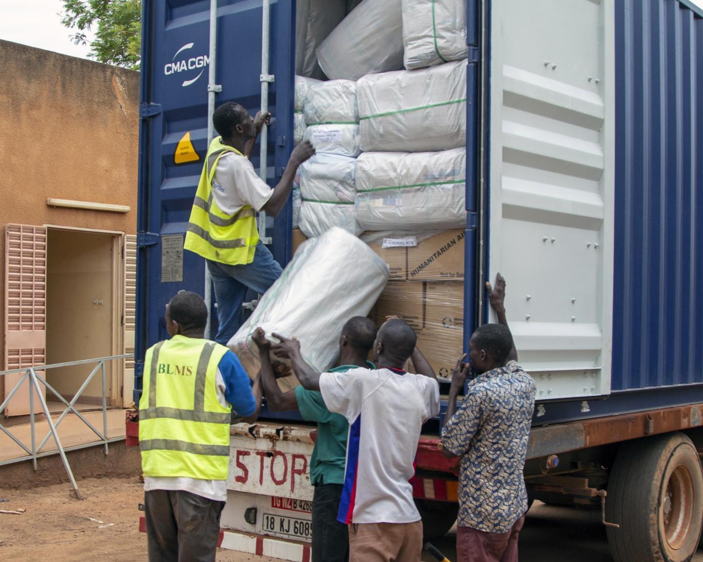 Five men, two of whom are in yellow reflective vests, unpack a shipping container