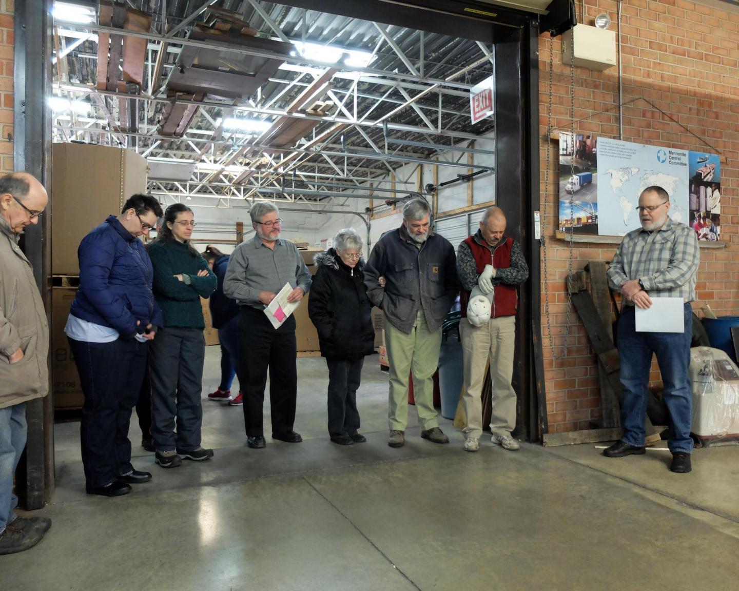A group of people stand in a warehouse and pray