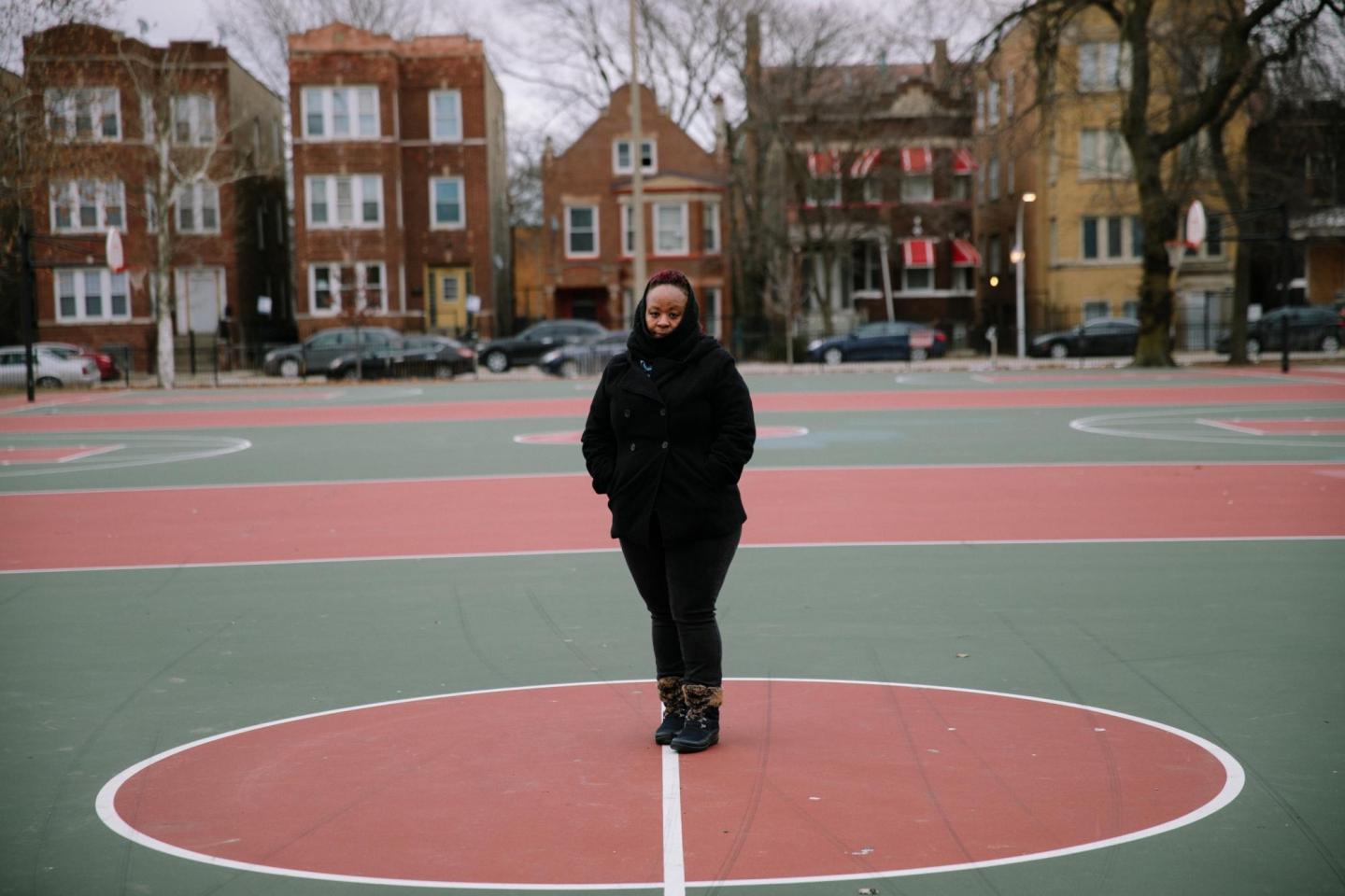 A woman stands in the middle of a basketball court at a city park.