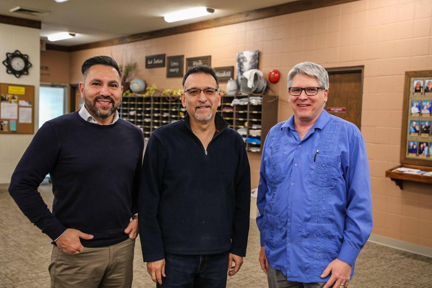 Three men stand in a row and smile for the camera.