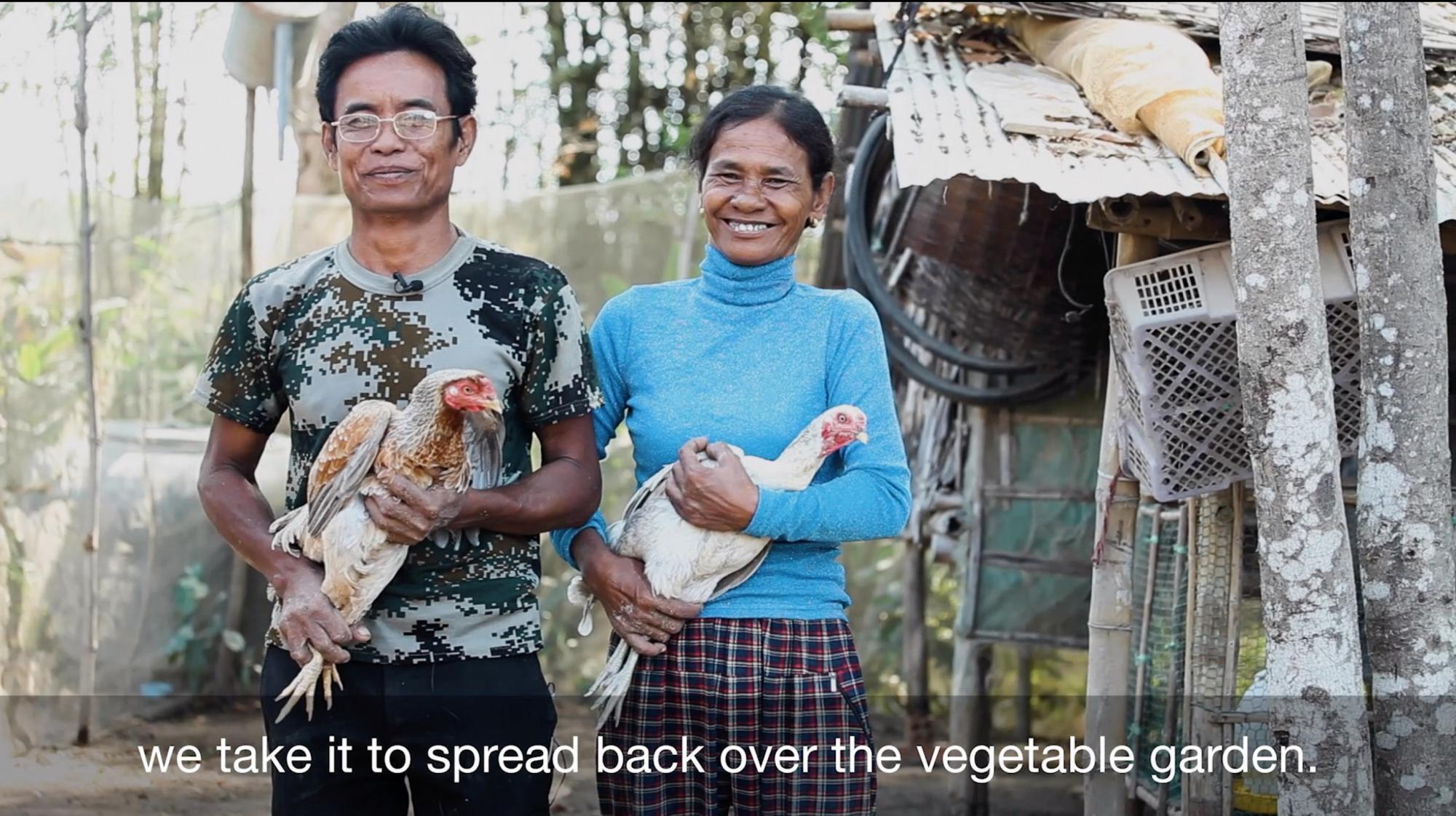 A screenshot from a video of a Cambodian man and woman holding chickens