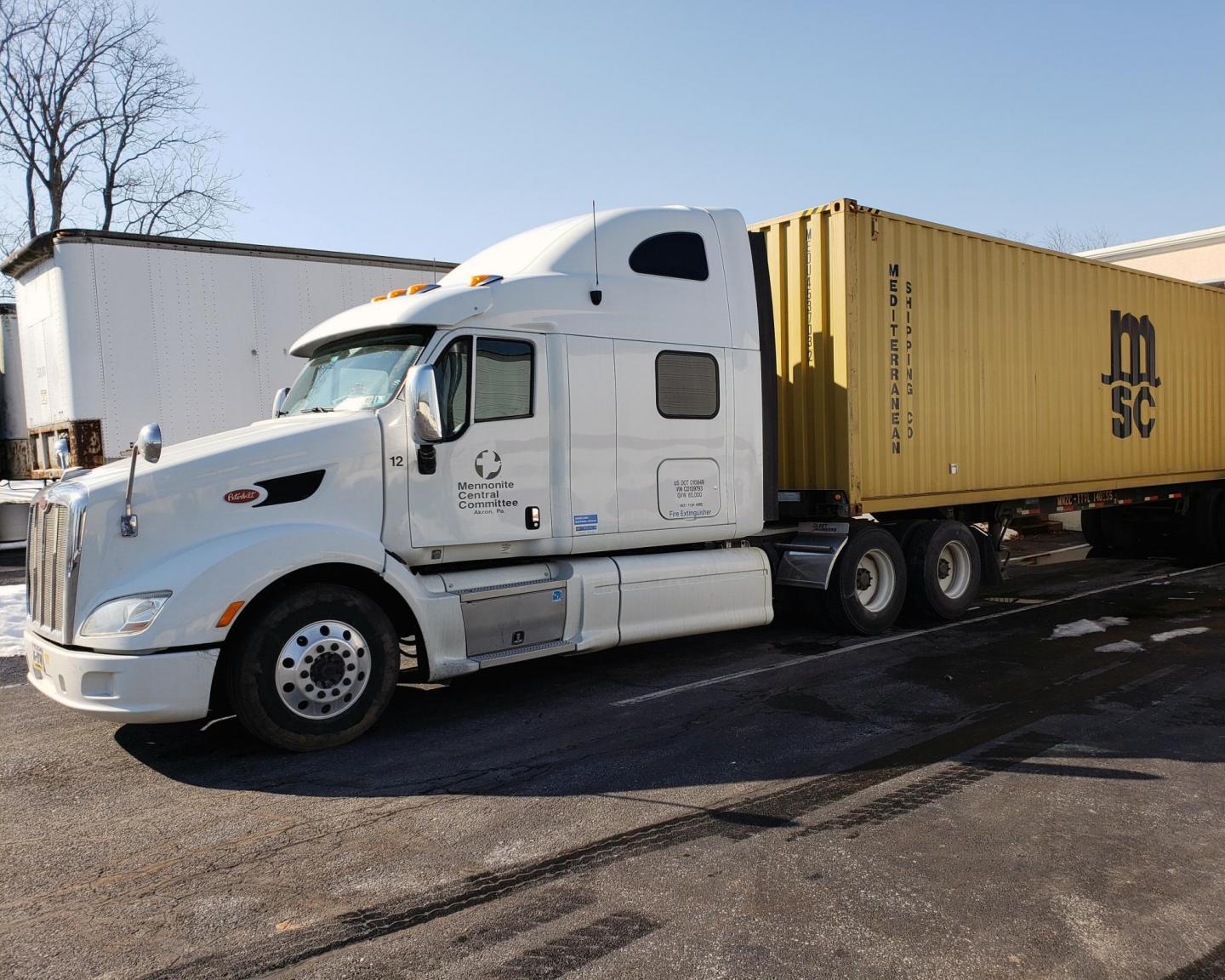 A semi truck with a white cab and a yellow trailer