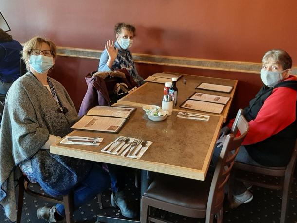 Three women with face masks sit together at a table in a restaurant 