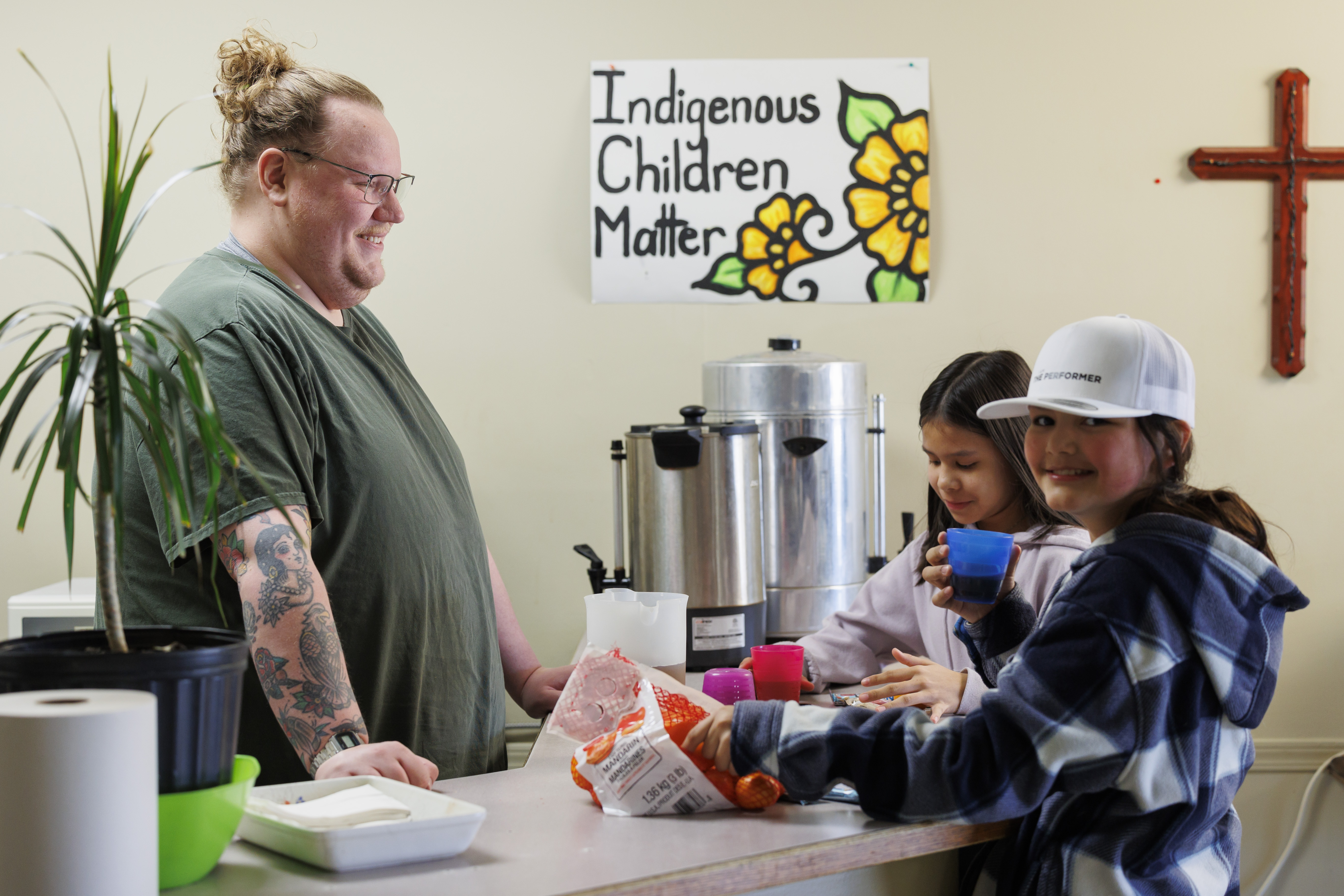 A person behind a counter serves drinks to two young girls who are helping themselves to oranges